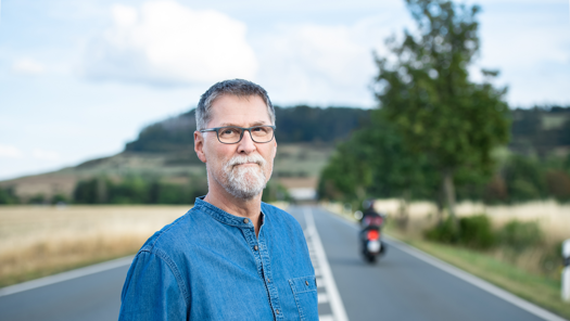 Jörg Fricke steht mitten auf einer Straßenfahrbahn. Im Hintergrund fährt ein Motorrad davon.