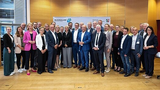 ©MSB NRW / Mark Hermenau Gruppe von Menschen posiert vor einer Flagge des Bildungslandes NRW
