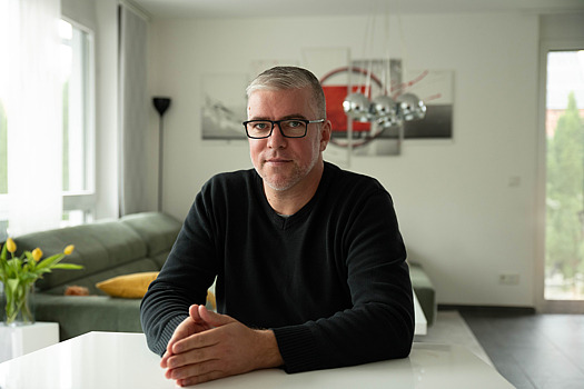 Florian Drechsler sitzt am Tisch in einem Wohnzimmer.