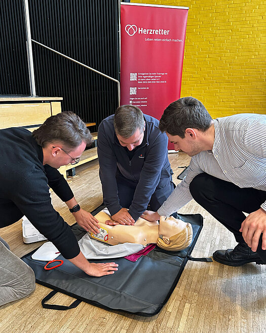 3 Männer üben Herz-Lungen-Massage an einer Puppe