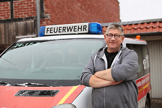 Dirk Wiezer mit verschränkten Armen neben einem Feuerwehr-Rettungswagen.