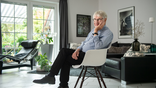 Werner Fritzsche sitzt mit demn Kopf auf seinen Arm gelehnt auf einem Stuhl in einem hellen Wohnzimmer.